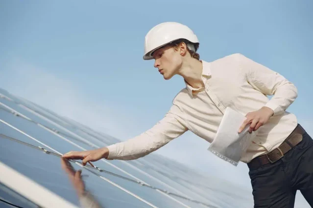 Persoană echipată profesional care inspectează panouri fotovoltaice pentru o centrală de 5 kW, cu documentație tehnică în mână